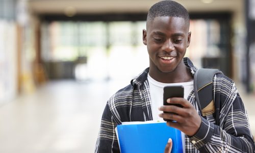 Male College Student Reading Text Message On Mobile Phone